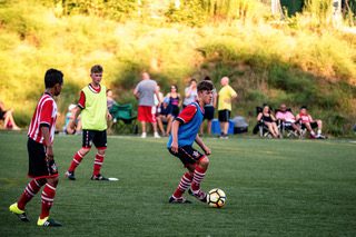 Youth flag football players competing indoors on turf field.