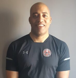 A man in black shirt standing next to wall.
