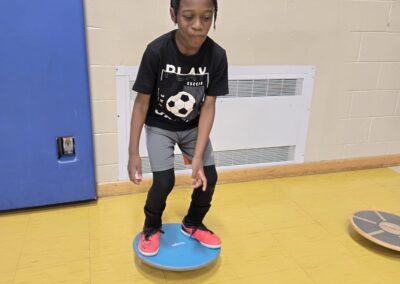 A young girl balancing on a blue wobble board indoors.