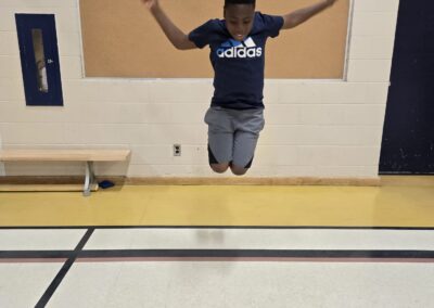 Person jumping in a gymnasium with arms raised.