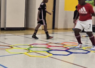 Two boys playing indoor soccer on a gym floor with colorful hexagonal patterns.