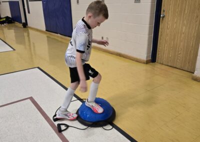 A child balances on a wobble board in a gym.
