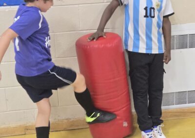 A child kicks a red punching bag while another child watches.