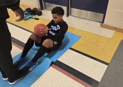 Child doing sit-ups while holding a basketball indoors.