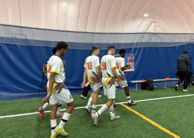 Young soccer players walking on an indoor field wearing white and yellow uniforms.