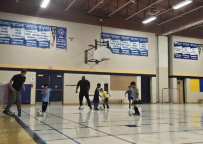 Kids playing basketball in a gym under adult supervision.
