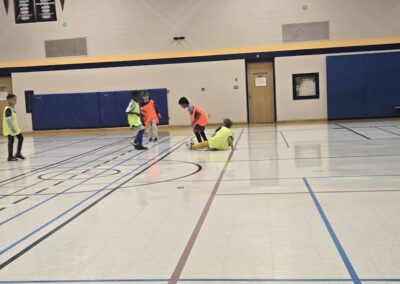 Children playing floor hockey in a gymnasium wearing safety gear.