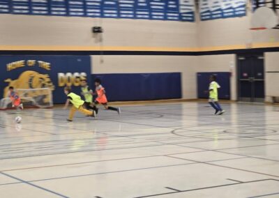 Children playing indoor soccer in a gymnasium.