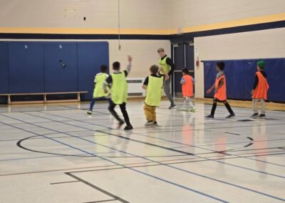 Kids playing basketball indoors in neon and orange jerseys.