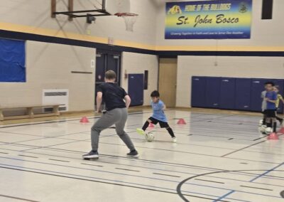 A young boy practices basketball moves with a coach in an indoor gym.
