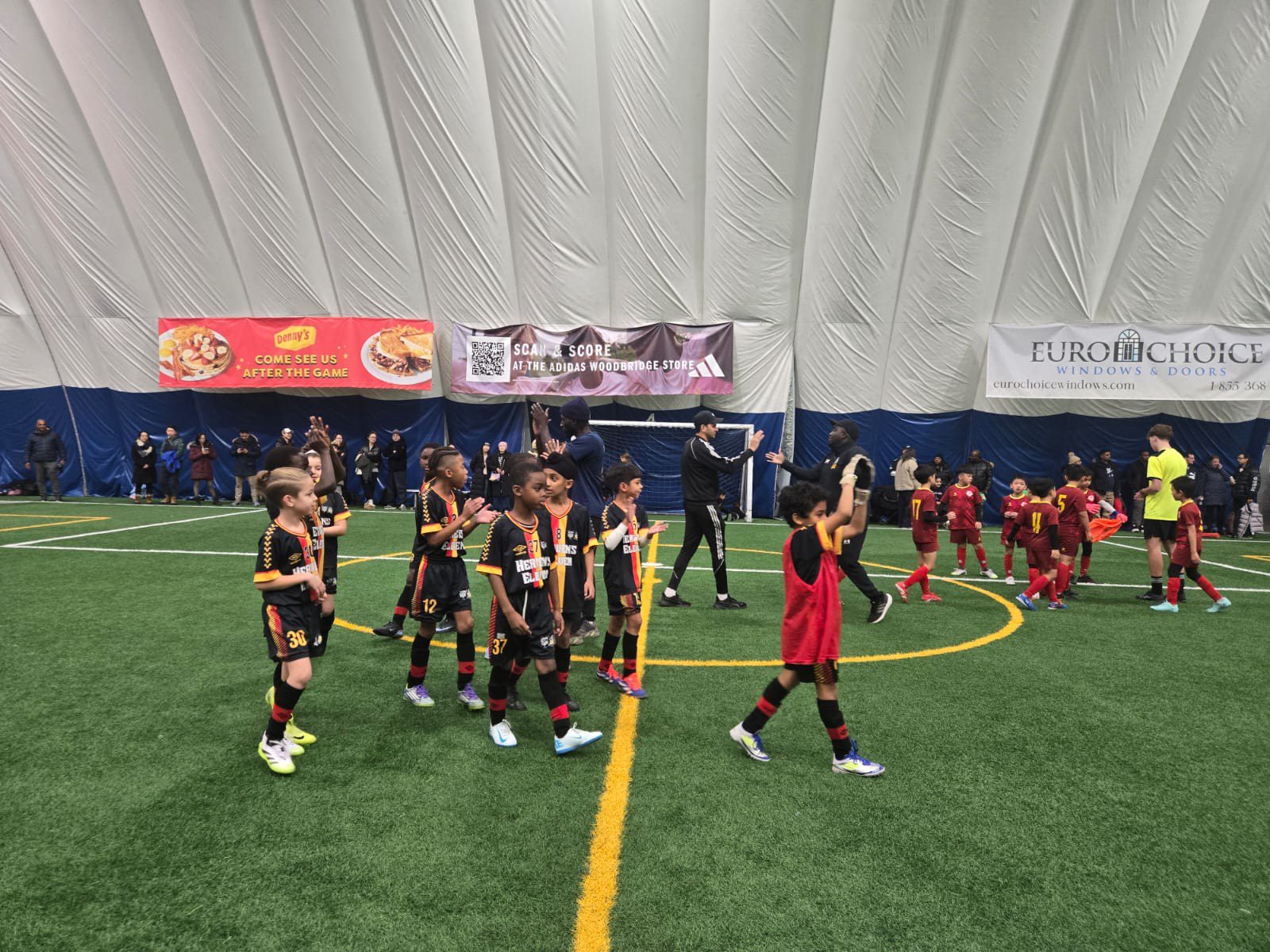 Youth flag football players competing indoors on turf field.