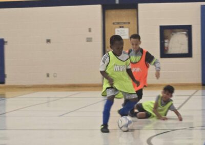Children playing soccer indoors, focused on the ball.