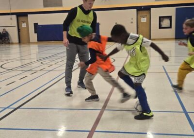 Three boys playing indoor soccer in a gymnasium.