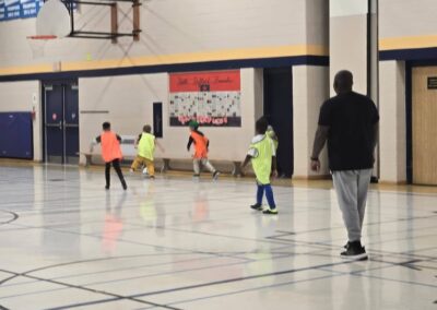 Kids playing indoor soccer with a coach watching closely.