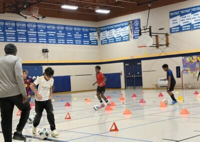 Kids practicing soccer drills indoors with cones in a gym.