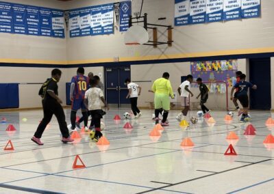 Kids practicing basketball drills with cones in a gymnasium.