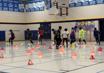 Kids practicing soccer drills indoors with cones.