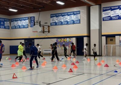 Children practicing basketball drills in a gym with orange cones.