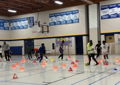 Kids practicing basketball drills with cones in a school gym.