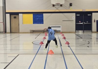 A child dribbling a basketball through cones in a gym.