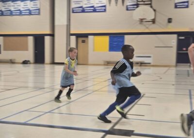 Two kids playing basketball in a gymnasium.
