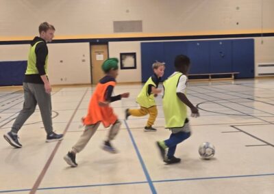 Kids playing indoor soccer, chasing the ball eagerly.