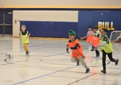 Kids playing indoor basketball in bright jerseys.