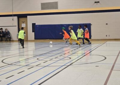 Children playing indoor soccer in a gymnasium.