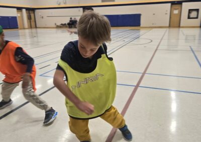 Young boy playing hockey indoors wearing a yellow vest.