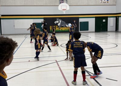 Kids playing basketball in a gymnasium wearing black and yellow uniforms.