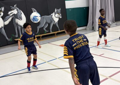 Young boys play indoor soccer wearing matching uniforms.