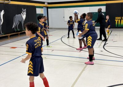 Children in sports uniforms practicing basketball drills in a gym.