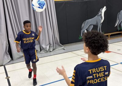 Two boys in basketball jerseys playing with a basketball indoors.