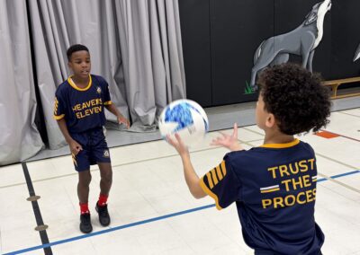 Two boys in matching sports jerseys pass a basketball indoors.