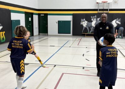 Kids playing basketball with a coach in a school gym.