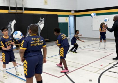 Children playing volleyball indoors in matching sports uniforms.
