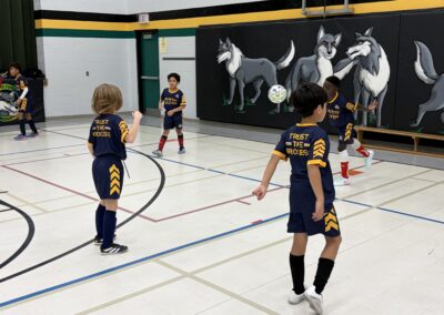Kids in sports uniforms jump rope in a gym with a wolf mural on the wall.