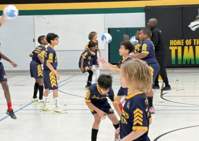 Young children playing basketball in a gym with a coach.
