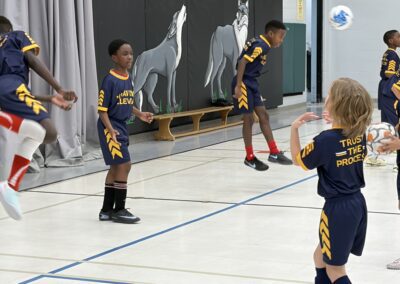 Young children playing indoor soccer in a gymnasium.