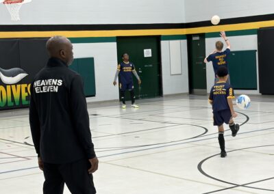 A coach observes basketball players practicing on a court.