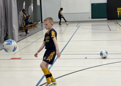 Young boy in yellow and black uniform playing indoor soccer.