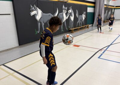 Child practicing soccer skills indoors with a ball mid-air.