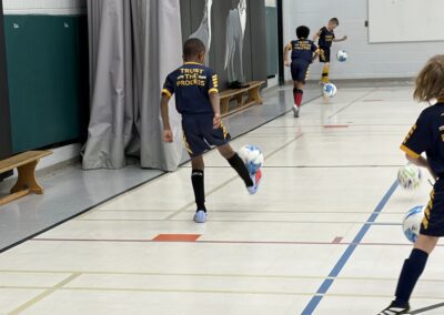 Young boys playing soccer indoors, one kicking the ball.