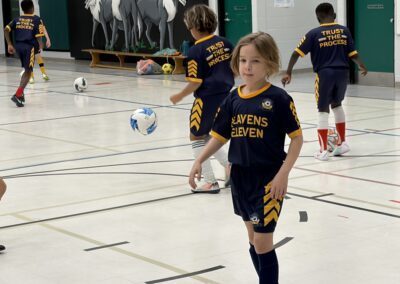Young kids playing indoor soccer, one girl in focus with soccer ball.