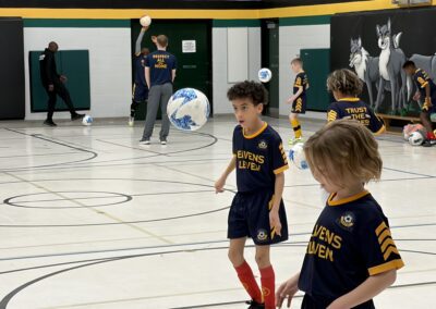 Children playing soccer indoors wearing blue and yellow uniforms.