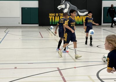 Young boys playing indoor soccer in a gymnasium.