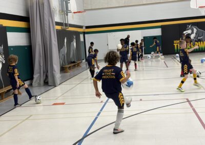 Young kids playing indoor soccer in a gymnasium.