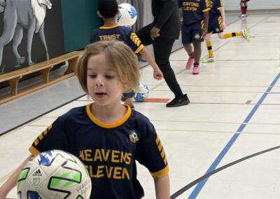 Young child in a sports jersey holding a soccer ball indoors.