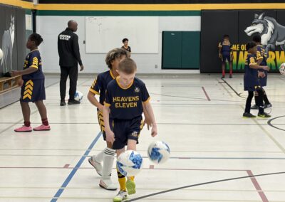 Young soccer player dribbling a ball in a gym.