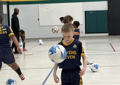 Young boy in a sports uniform holding a soccer ball indoors.